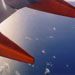 Dramatic red of the plane's wing contrasted to the white and blue of clouds and sea.